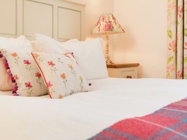 A bed with floral cushions and a bedside table with a floral lamp at Ardlarach Lodge in Cullipool Isle Of Luing