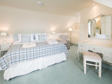 A bedroom with a large bed with bedside tables lamps an armchair a floor lamp a dressing table with mirror and stool at Ardlarach Lodge in Cullipool Isle Of Luing