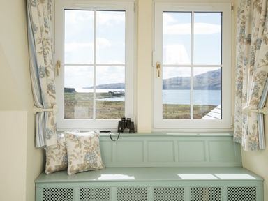 A window seat with floral cushions and curtains with a view of water and hills at Ardlarach Lodge in Cullipool Isle Of Luing