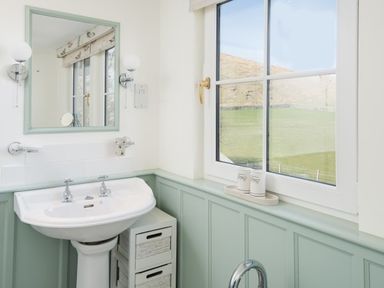 A bathroom with a pedestal sink mirror wall sconces a window and a small drawer unit at Ardlarach Lodge in Cullipool Isle Of Luing