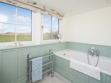 A bathroom with a bathtub under two windows and a towel rack with towels at Ardlarach Lodge in Cullipool Isle Of Luing