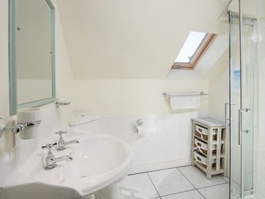 A bathroom with a sink a mirror a toilet a towel rack a storage unit with baskets and a glass shower enclosure at Ardlarach Lodge in Cullipool Isle Of Luing