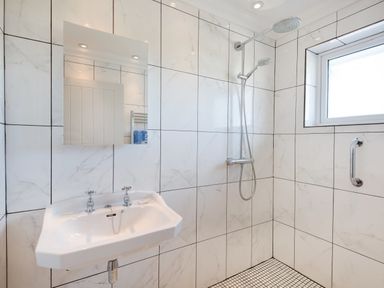 A bathroom with a wall-mounted sink a mirror a shower head a window and tiled walls and floor at Ardlarach Lodge Cullipool Isle Of Luing
