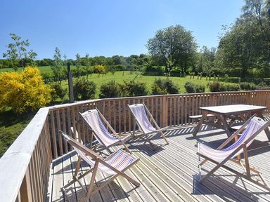 A wooden deck with four striped deckchairs and a wooden picnic table overlooking a grassy field with trees at Skylarks in Ferintosh near to Dingwall