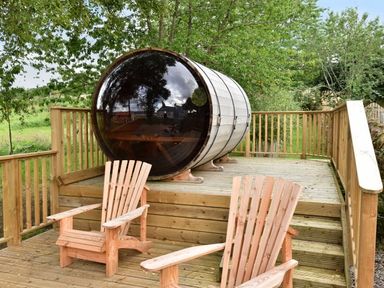 A wooden deck with two wooden chairs and a barrel-shaped pod surrounded by trees at Skylarks in Ferintosh near to Dingwall