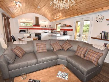 A living room with a grey sectional sofa and plaid cushions opening to a kitchen and dining area with wooden ceiling at Skylarks in Ferintosh near to Dingwall