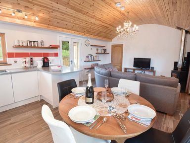 A kitchen and dining area with a round wooden table set for four next to a gray sofa and a TV at Skylarks Ferintosh near to Dingwall