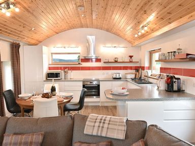 A kitchen and dining area with a wooden ceiling a round table set for four and kitchen appliances at Skylarks in Ferintosh near to Dingwall