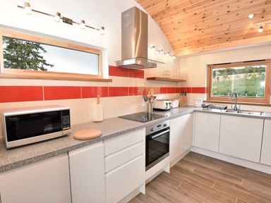 A kitchen with white cabinets a microwave an oven a toaster and two windows at Skylarks Ferintosh near to Dingwall