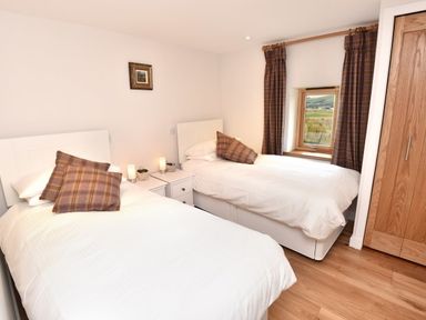 A bedroom with two single beds white bedding plaid pillows nightstand wooden wardrobe and window with plaid curtains at Skylarks in Ferintosh near to Dingwall