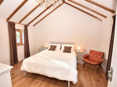 A bedroom with a double bed bedside tables an orange armchair wooden floor and wooden beams on the ceiling at Skylarks Ferintosh near to Dingwall