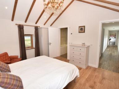 A bedroom with a bed pillows a chest of drawers an armchair window with curtains and exposed beams at Skylarks in Ferintosh near to Dingwall