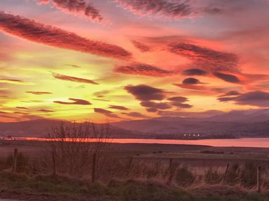 A sunset over hills with a body of water and fields with a fence in the foreground at Skylarks in Ferintosh near to Dingwall