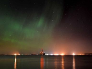 Night sky with northern lights over water with an oil rig and distant lights at Skylarks in Ferintosh near to Dingwall