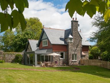 A stone house with a slate roof and a patio table with an umbrella in a garden at Beltie Lodge in Borgue