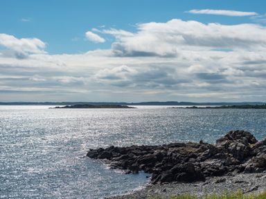 A rocky shoreline with water and small islands under a partly cloudy sky at Beltie Lodge in Borgue