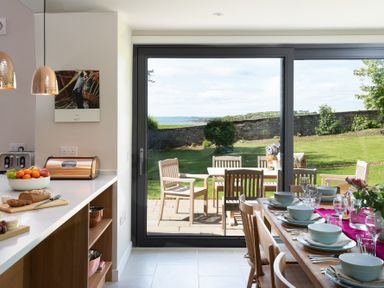 A kitchen and dining area with set table and outdoor patio furniture visible through glass doors at Beltie Lodge in Borgue