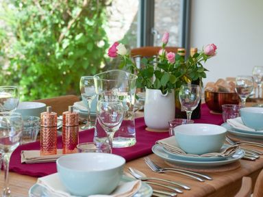 A dining table set with bowls plates cutlery glassware a water jug flowers and bread at Beltie Lodge in Borgue