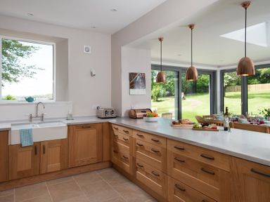 A kitchen with wooden cabinets a white countertop copper pendant lights and a dining area with glass doors at Beltie Lodge in Borgue