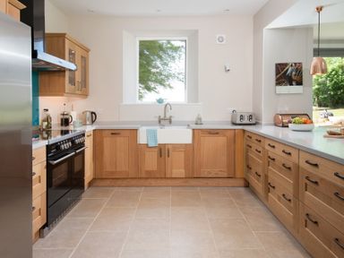 A kitchen with wooden cabinets a black stove a white sink and a window at Beltie Lodge in Borgue