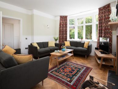 A living room with three dark sofas yellow cushions a wooden coffee table a colorful rug and a television at Beltie Lodge in Borgue