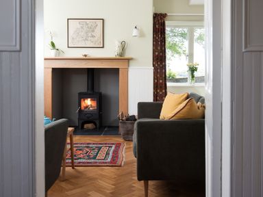 A living room with a wood burning stove a rug sofas with cushions and a window with flowers at Beltie Lodge Borgue