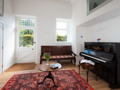 A sitting room with a piano a wooden bench and a round table with flowers at Beltie Lodge in Borgue