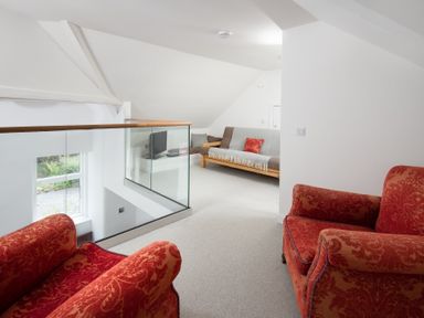 A sitting area with red armchairs and a sofa with a TV on a stand at Beltie Lodge in Borgue