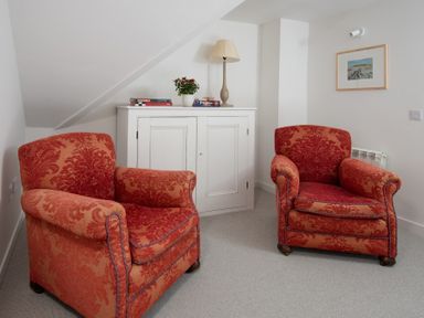A room with two red patterned armchairs a white cabinet with books a lamp and a plant at Beltie Lodge in Borgue