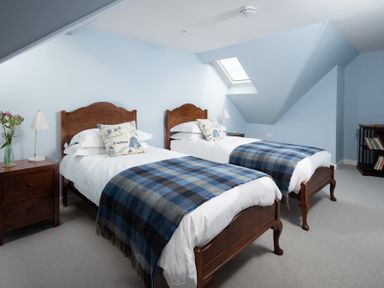 A bedroom with two single wooden beds with blue checkered blankets and bedside tables at Beltie Lodge in Borgue