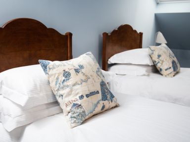 Two beds with wooden headboards white bedding and decorative pillows with map designs at Beltie Lodge in Borgue