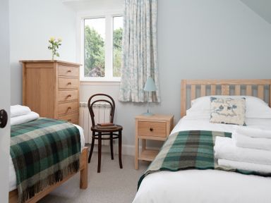 A bedroom with two single beds a wooden dresser a wooden chair and a wooden nightstand at Beltie Lodge in Borgue
