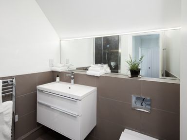 A bathroom with a white sink vanity a large mirror folded towels a potted plant and a towel rack at Beltie Lodge in Borgue