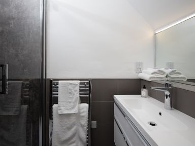 A bathroom with a sink, faucet, mirror, towel rack with towels, and a glass shower door at Beltie Lodge in Borgue