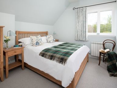 A bedroom with a wooden bed with white bedding green plaid blanket two bedside tables with lamps and flowers near a window at Beltie Lodge in Borgue
