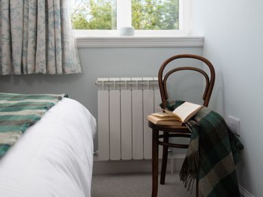 A chair with an open book and a blanket next to a bed under a window at Beltie Lodge in Borgue