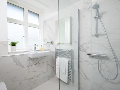 A bathroom with a wall-mounted sink and a shower with a handheld showerhead at Beltie Lodge in Borgue