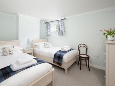 A bedroom with two single beds a small nightstand and lamp a wooden chair and a dresser with flowers at Beltie Lodge in Borgue