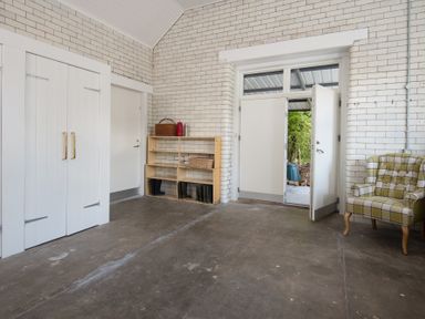 A room with white brick walls a double door a wooden shelf with boots a green plaid armchair at Beltie Lodge in Borgue