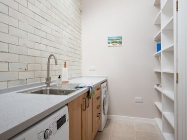 A utility room with a sink washing machines wooden cabinets and white shelving at Beltie Lodge in Borgue