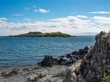 A rocky coastline with water and an island in the distance at Beltie Lodge in Borgue