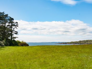 A grassy field with trees on the left and a body of water in the background at Beltie Lodge in Borgue