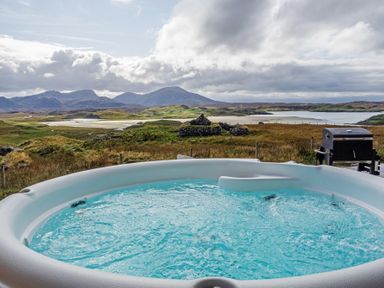 An outdoor hot tub with bubbling water overlooking a grassy landscape with hills and a body of water at Eagle Lodge in Uig near Stornoway