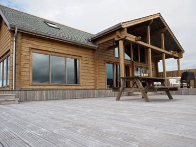 A wooden lodge with large windows a covered porch a picnic table and a deck at Eagle Lodge in Uig near Stornoway