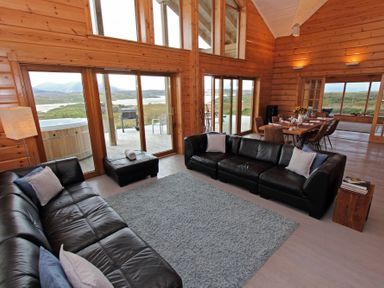 A living room with black leather sofas and a dining area with a wooden table at Eagle Lodge in Uig near Stornoway