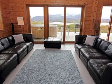 A living room with black leather sofas and a gray rug overlooking a patio with a hot tub at Eagle Lodge in Uig near Stornoway
