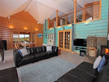A living room with black leather sofas a dining table and chairs wood burning stove and blue and wood paneled walls at Eagle Lodge Uig near Stornoway