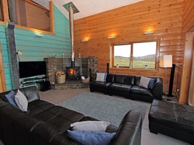 A living room with two black leather sofas a grey rug wood stove and a television at Eagle Lodge in Uig near Stornoway