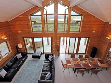 A wooden living and dining area with black sofas and a dining table with chairs at Eagle Lodge in Uig near Stornoway
