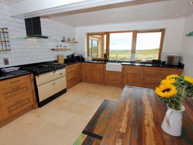 A kitchen with wooden cabinets a stove a large window and sunflowers in a jug on a wooden table at Eagle Lodge in Uig near Stornoway